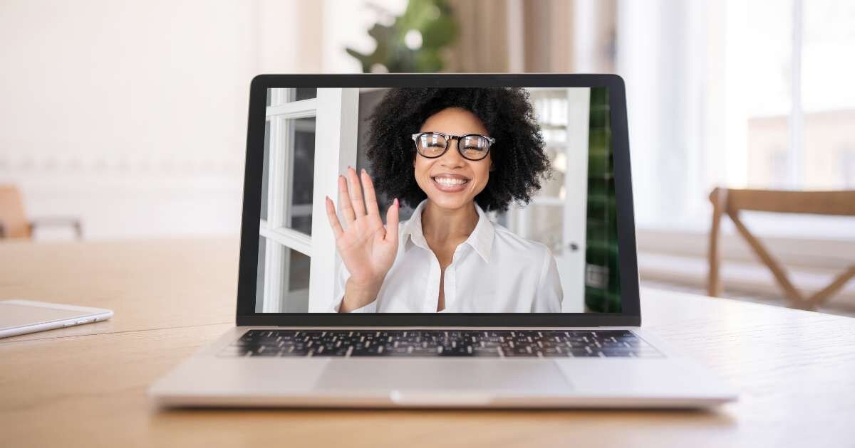 A remote meeting with a happy women waving hello through laptop screen 